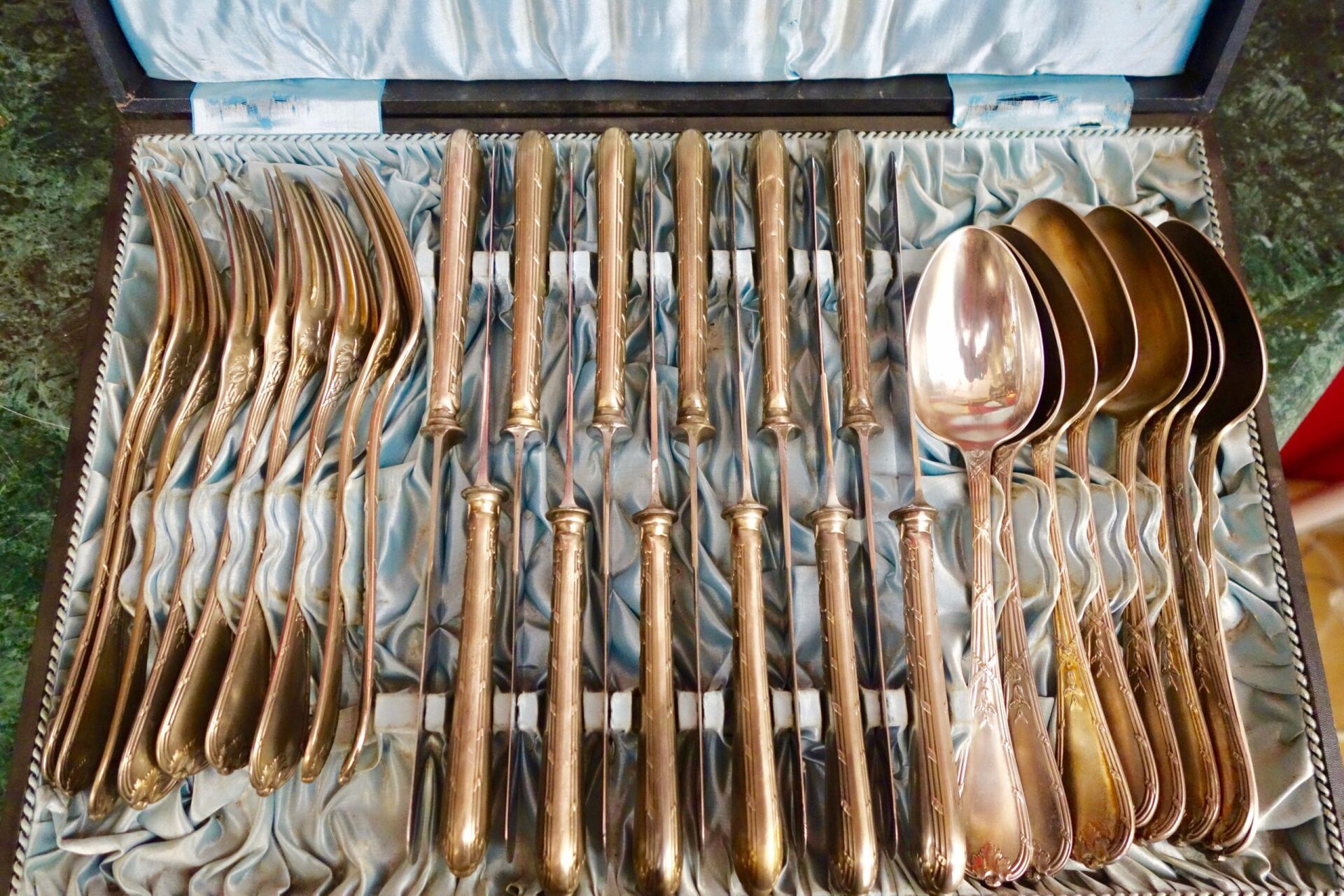 Silbernes Besteckset in einer ausgekleideten Schachtel; Gabeln, Messer, Löffel angeordnet.