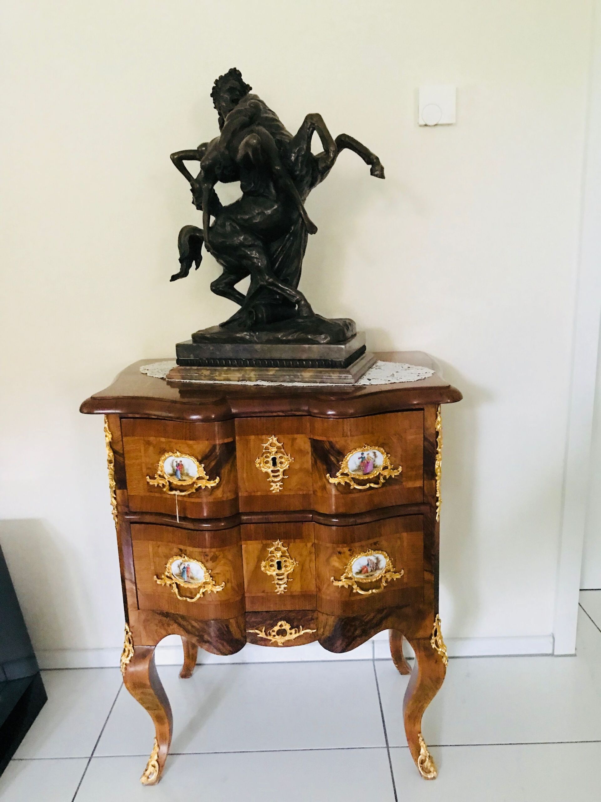 Eine dekorative Kommode aus Holz mit einer Bronzestatue eines Pferdes und Reiters darauf.