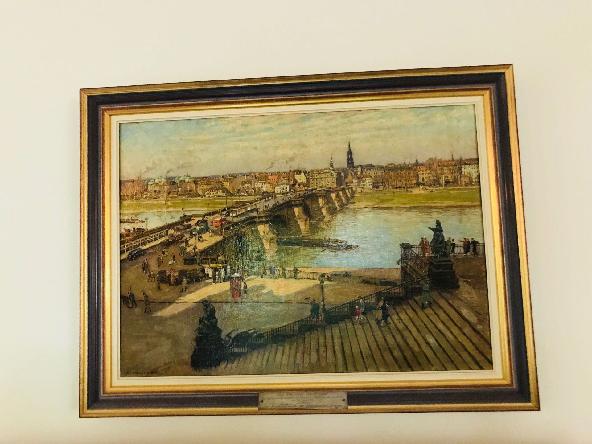 Gemälde einer Brücke über einen Fluss mit Gebäuden im Hintergrund. Gerahmt, an einer cremefarbenen Wand montiert.