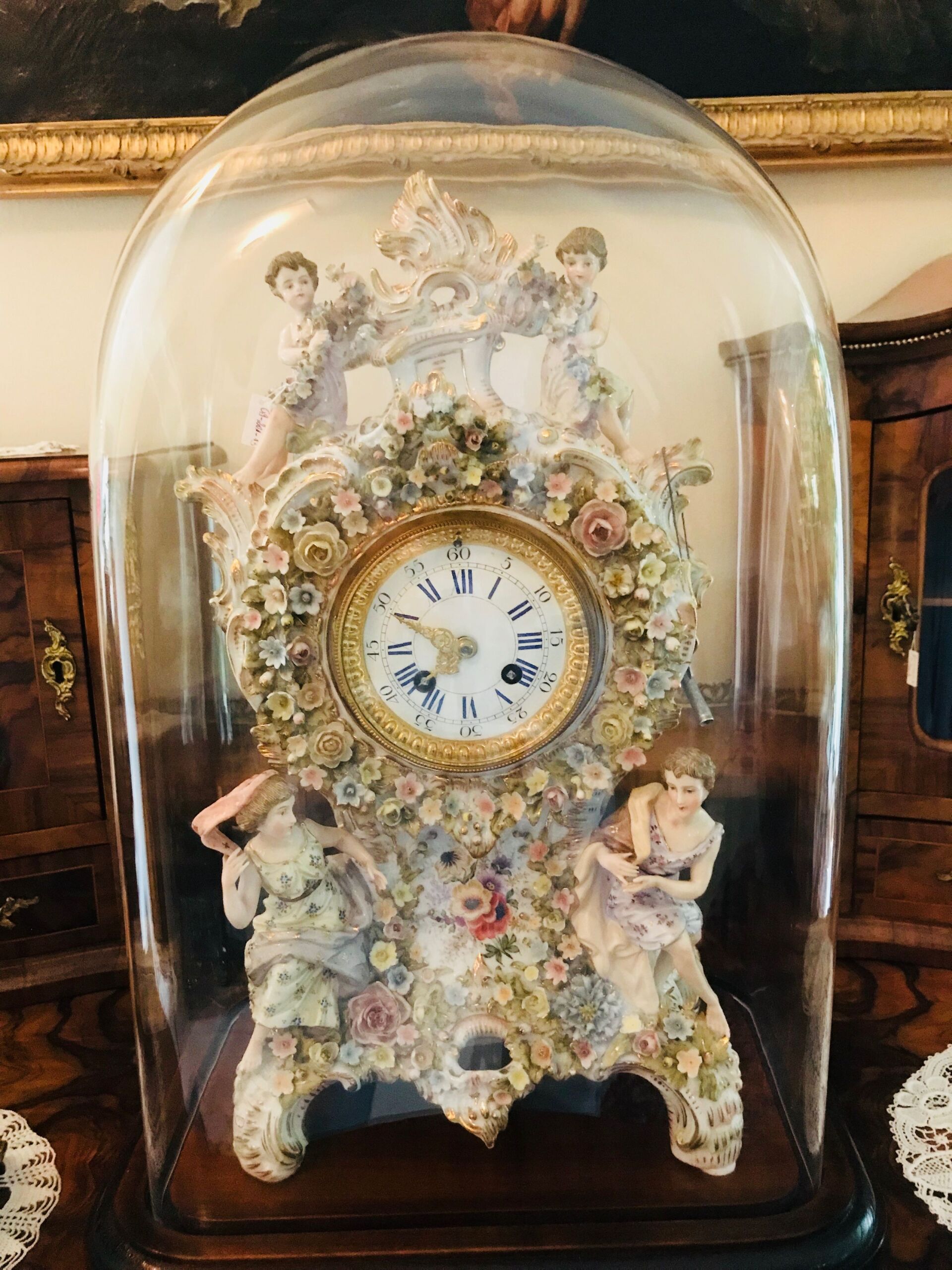 Uhr in einer Glaskuppel, verziert mit Blumen- und Engelsfiguren.