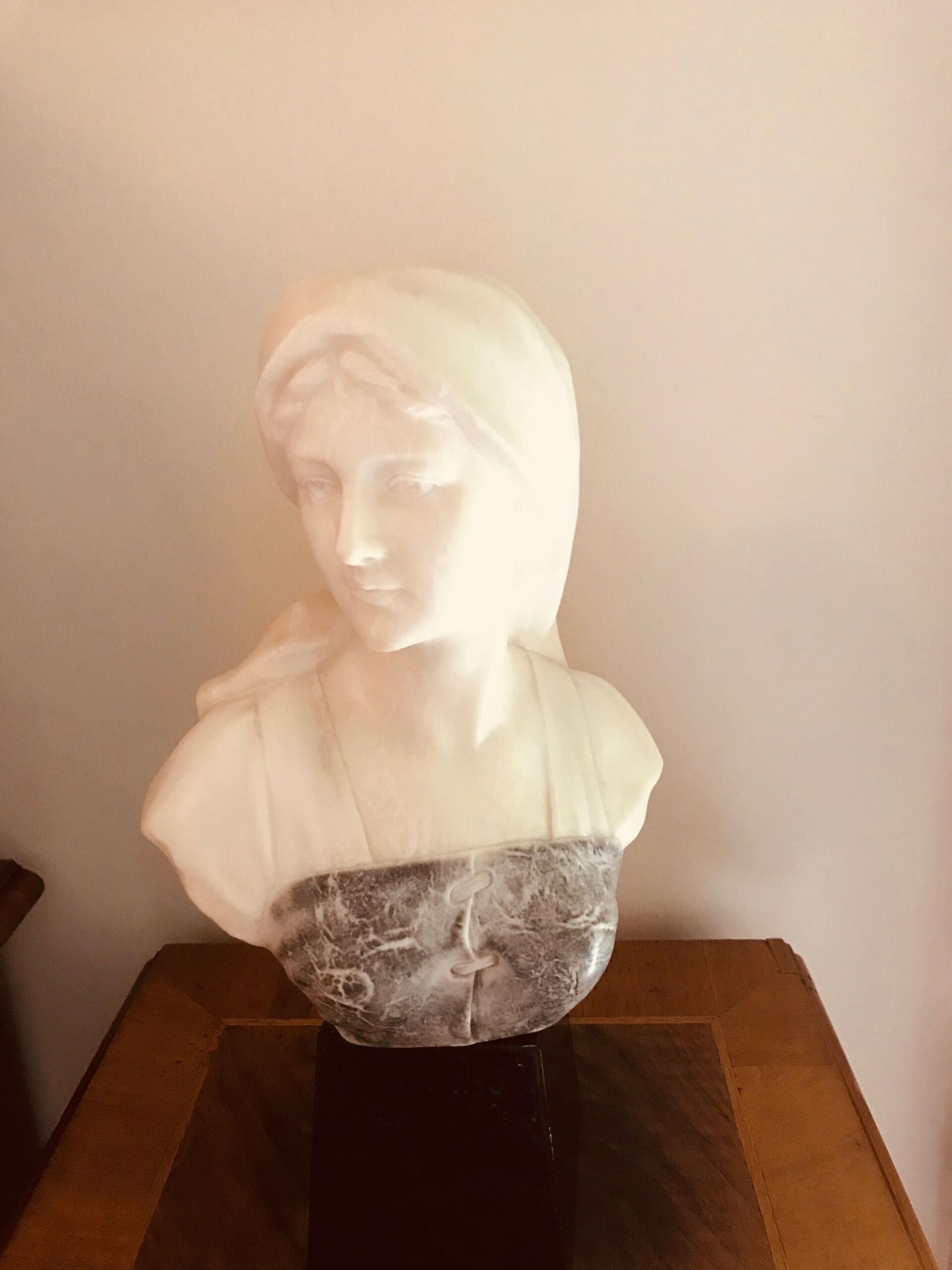 Marmorbüste einer Frau mit niedergeschlagenen Augen, die ein drapiertes Gewand trägt.