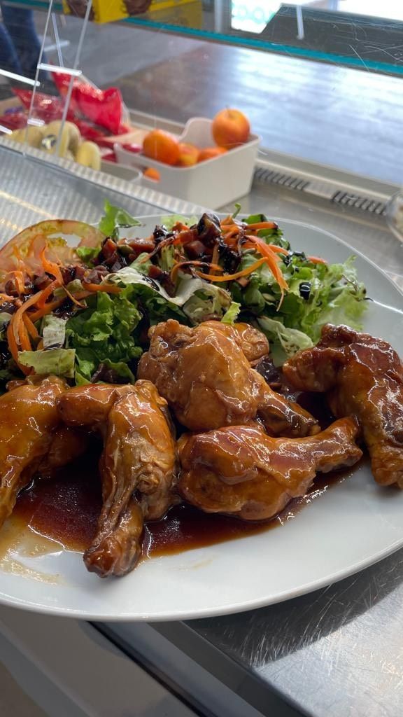 Un plato blanco cubierto con alitas de pollo y una ensalada sobre un mostrador.