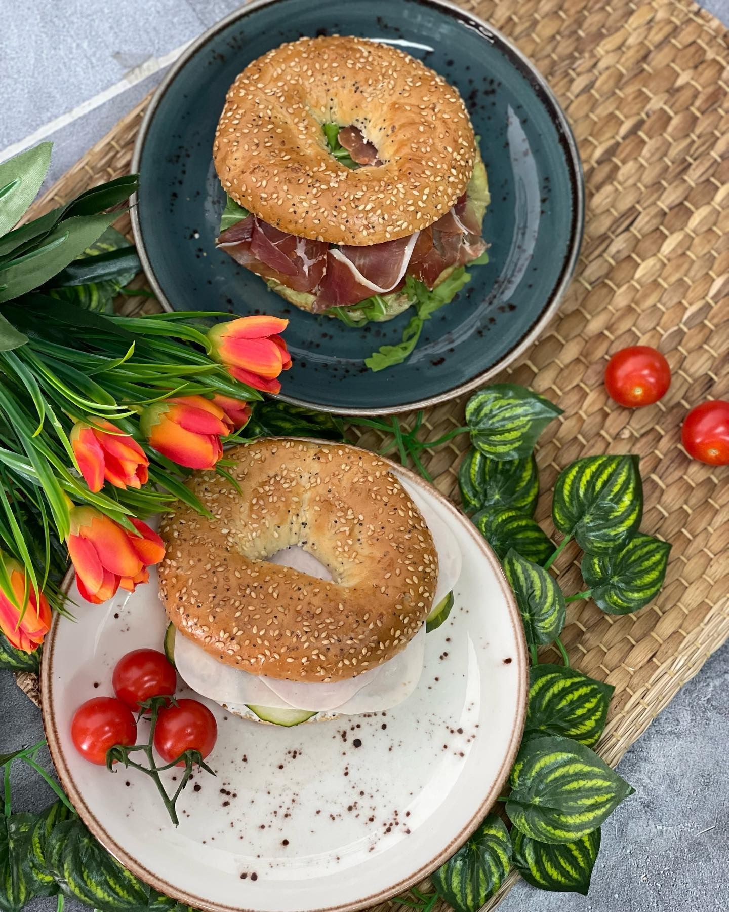 Dos platos de bagels con tomates y flores sobre una mesa.
