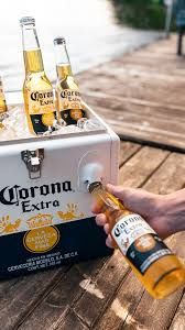 Glacière Corona remplie de glaçons et de bières Corona, posée sur un ponton en bois au bord de l'eau.