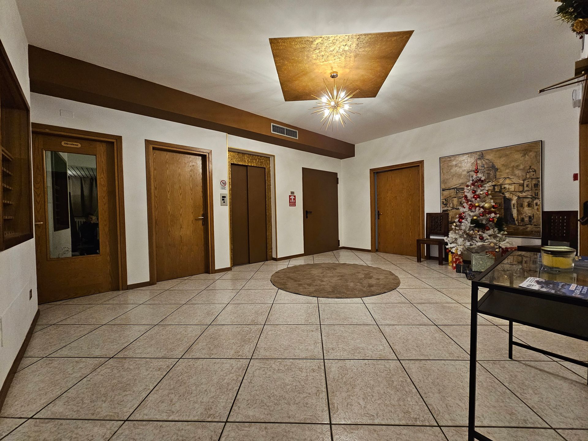 Hall con pavimento piastrellato, numerose porte in legno, ascensore e tappeto circolare.