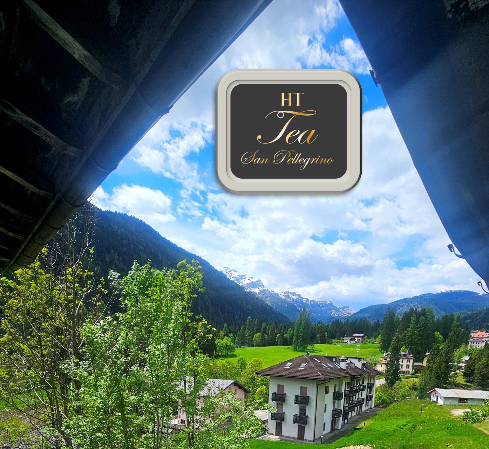 Vista panoramica di una valle con montagne, alberi verdi ed edifici, incorniciata da una struttura.