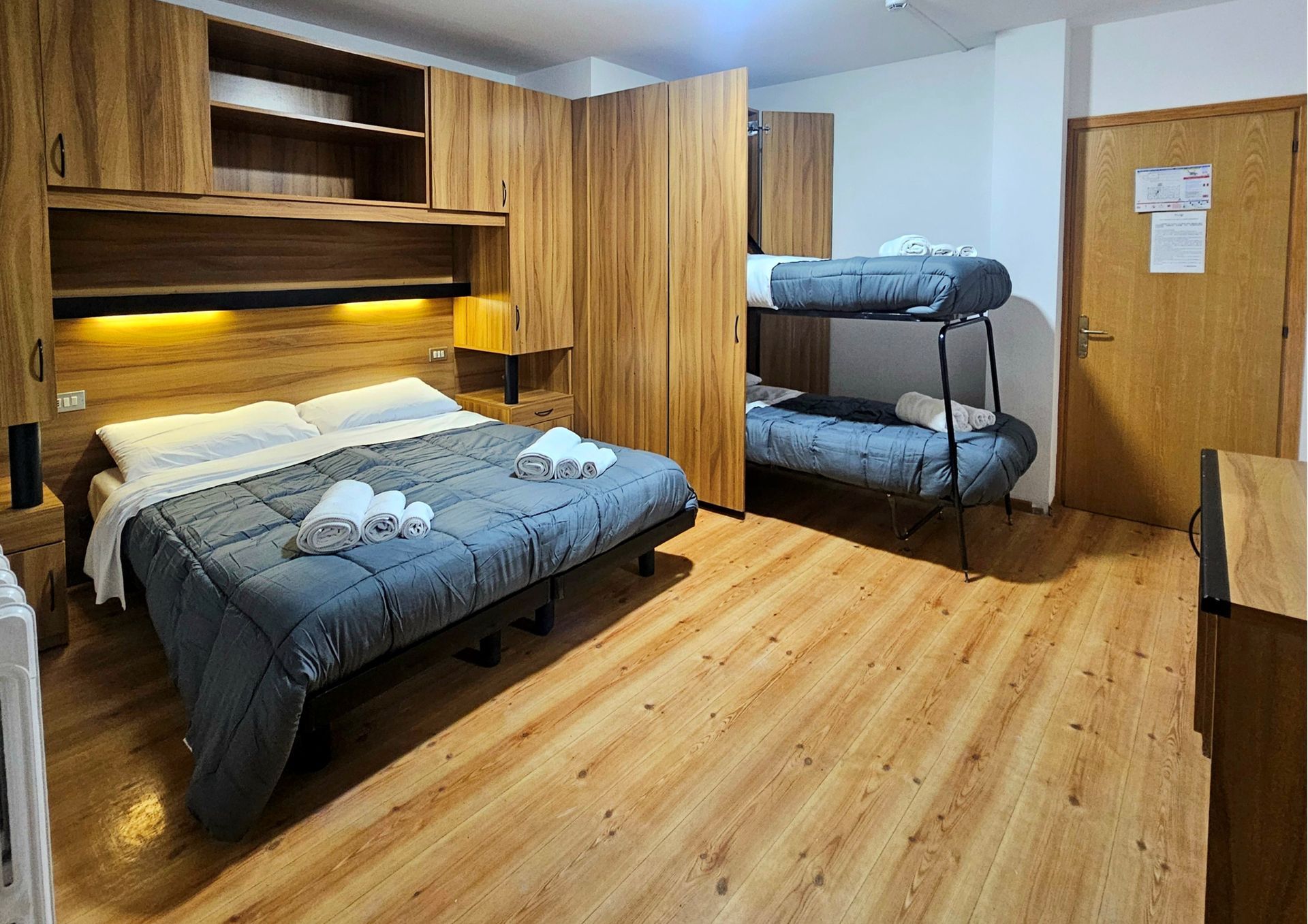 Piccola camera da letto con letto matrimoniale, letti a castello e pareti e pavimento rivestiti in legno.