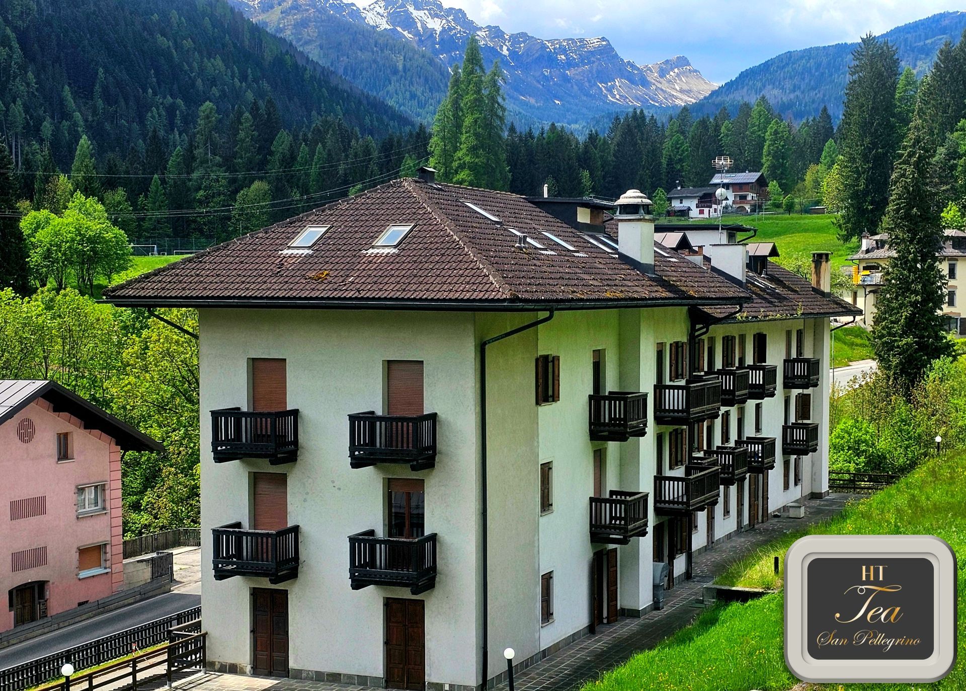 Edificio residenziale con balconi e tetto marrone, situato in una valle di montagna.