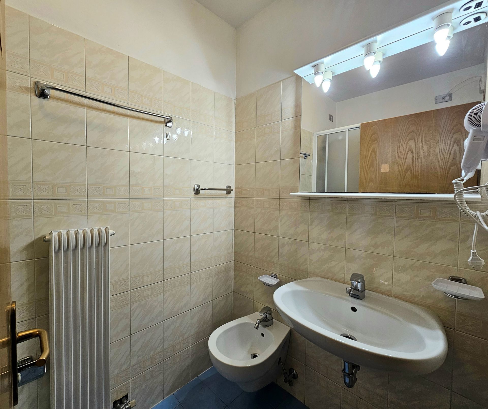 Piccolo bagno con pareti piastrellate beige, sanitari bianchi e un grande specchio.