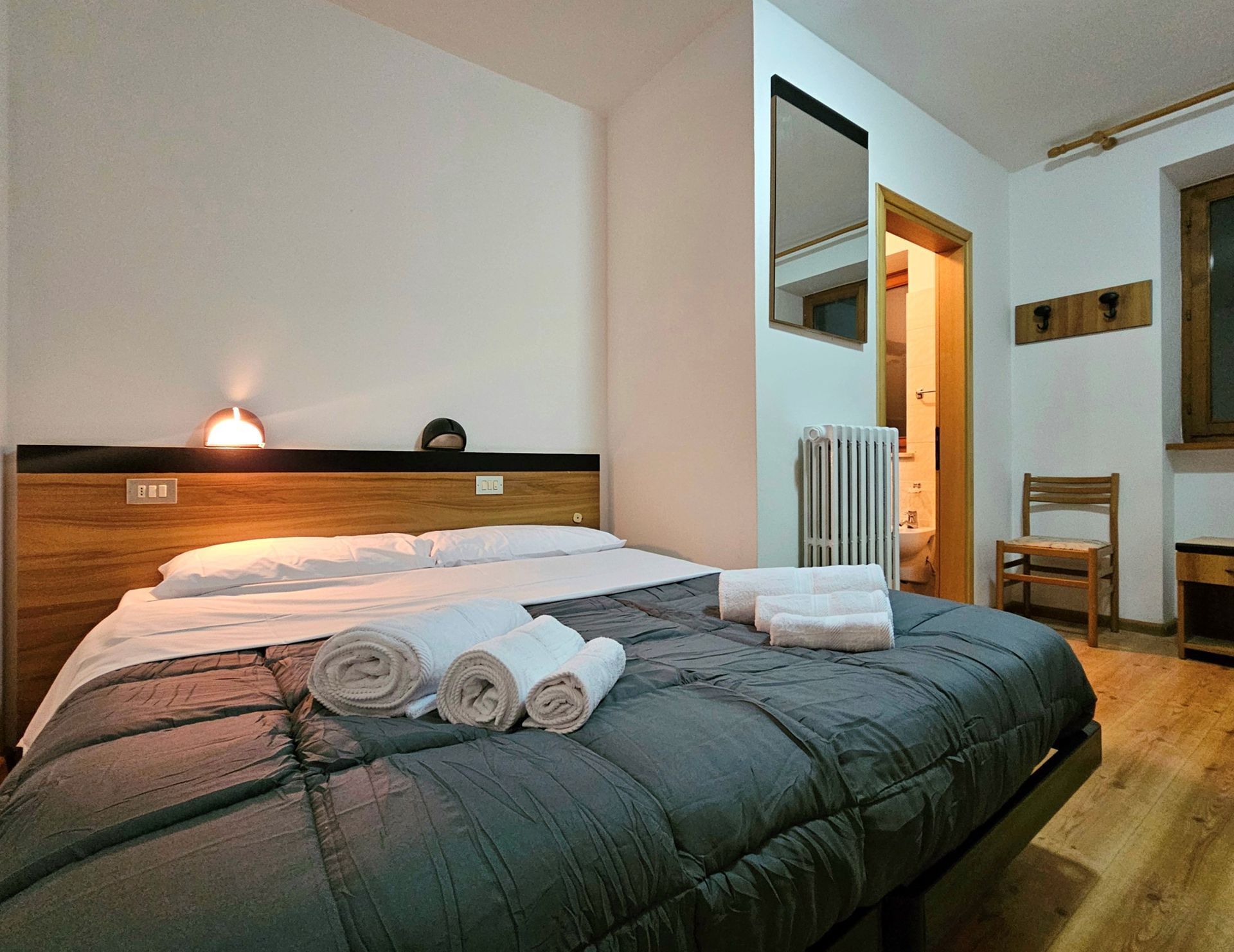 Camera da letto con un letto grande, asciugamani piegati e un piccolo bagno visibile.