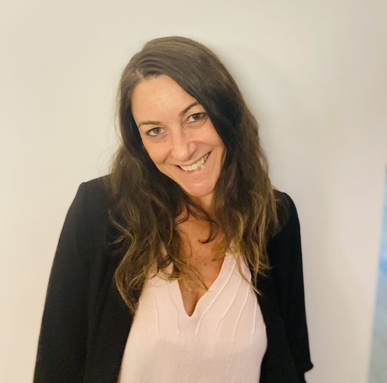 Una mujer con una camisa rosa y una chaqueta negra sonríe a la cámara.