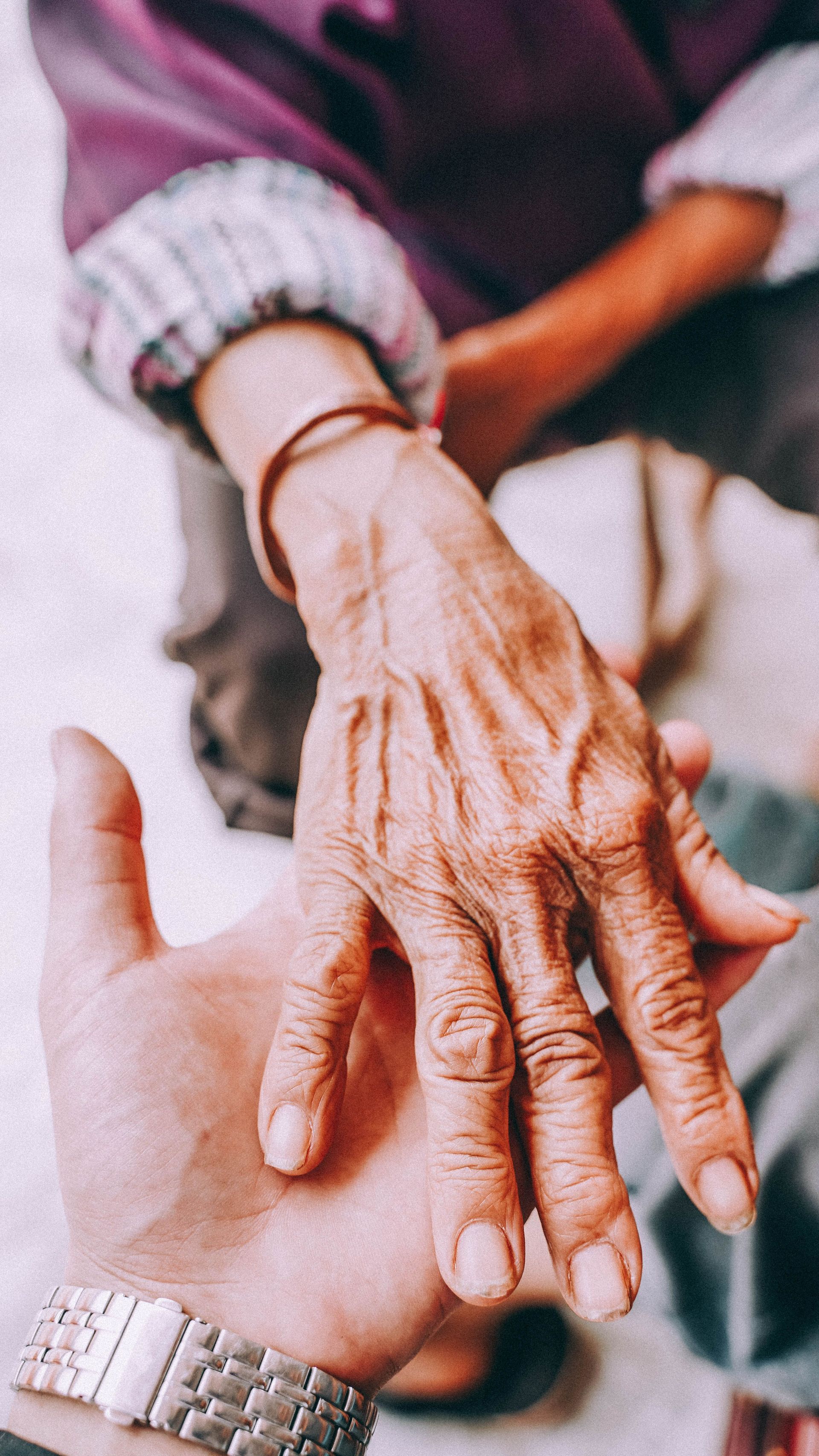 Deux mains jointes en signe de soutien, une main usée reposant sur la paume d'une personne plus jeune.