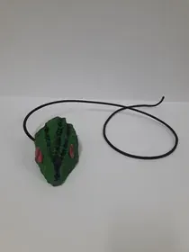 Un juguete verde con una cuerda negra atada a él está sentado sobre una superficie blanca.