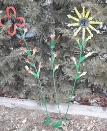 Tres flores de metal están sentadas frente a un árbol.