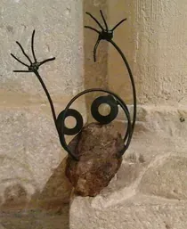 Una escultura de alambre de una rana sentada sobre una roca.