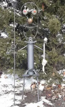 Una escultura de metal de un hombre parado frente a un árbol de Navidad.
