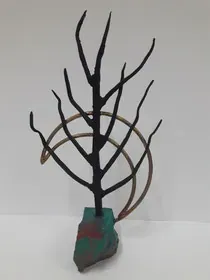 Una escultura de un árbol sin hojas está sentada encima de una roca.