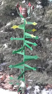 Un árbol de Navidad verde hecho de metal está sentado frente a un árbol de Navidad.