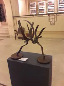 Una escultura de metal está sentada encima de un cubo negro en una habitación.