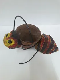 Una hormiga colorida sosteniendo una maceta sobre una superficie blanca.