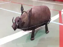 Una estatua de cerdo de metal está sentada en una cancha de baloncesto.