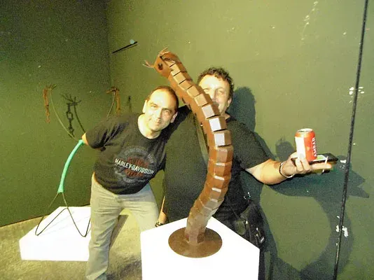 Dos hombres de pie junto a una escultura, uno de ellos sosteniendo una lata de Coca-Cola.