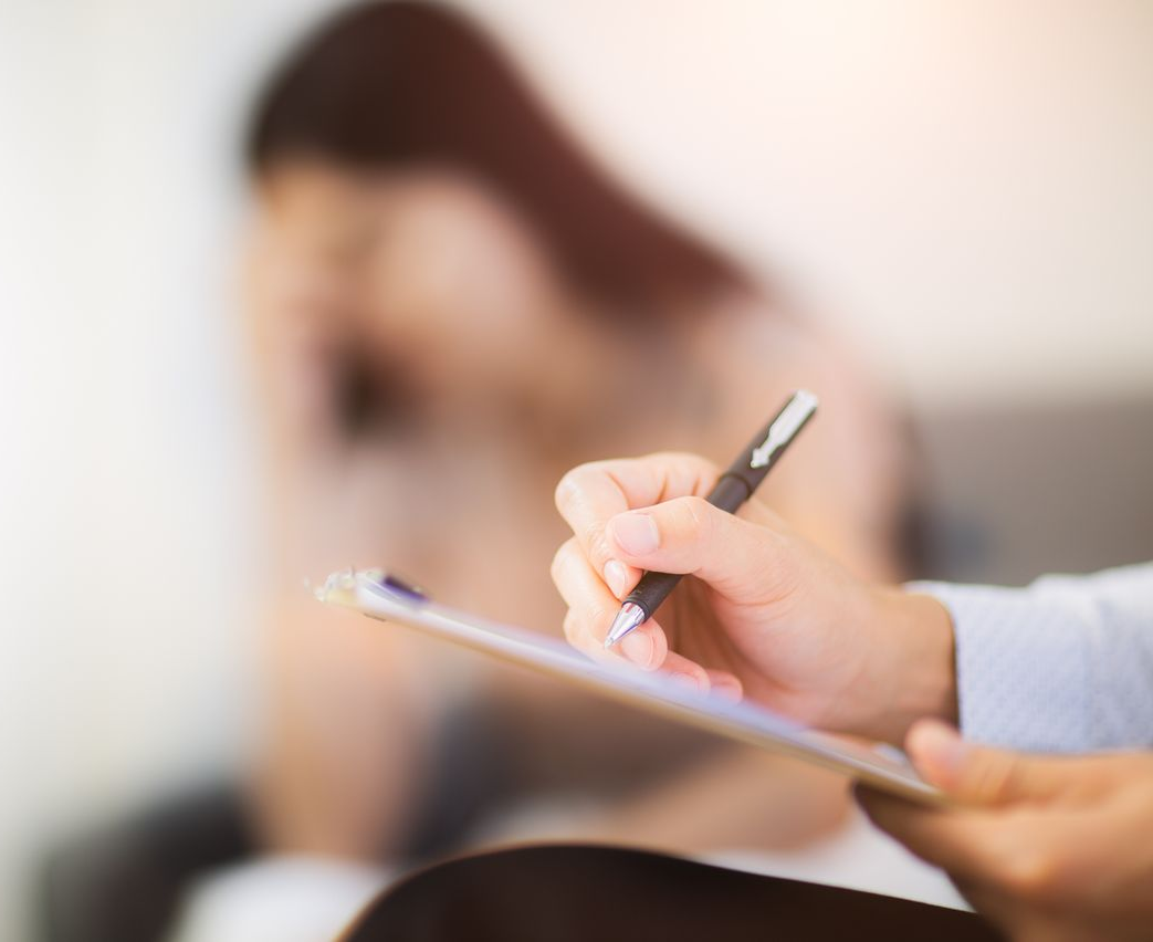 Une personne tenant un stylo et un bloc-notes, prenant des notes tandis qu'une autre personne a l'air triste.