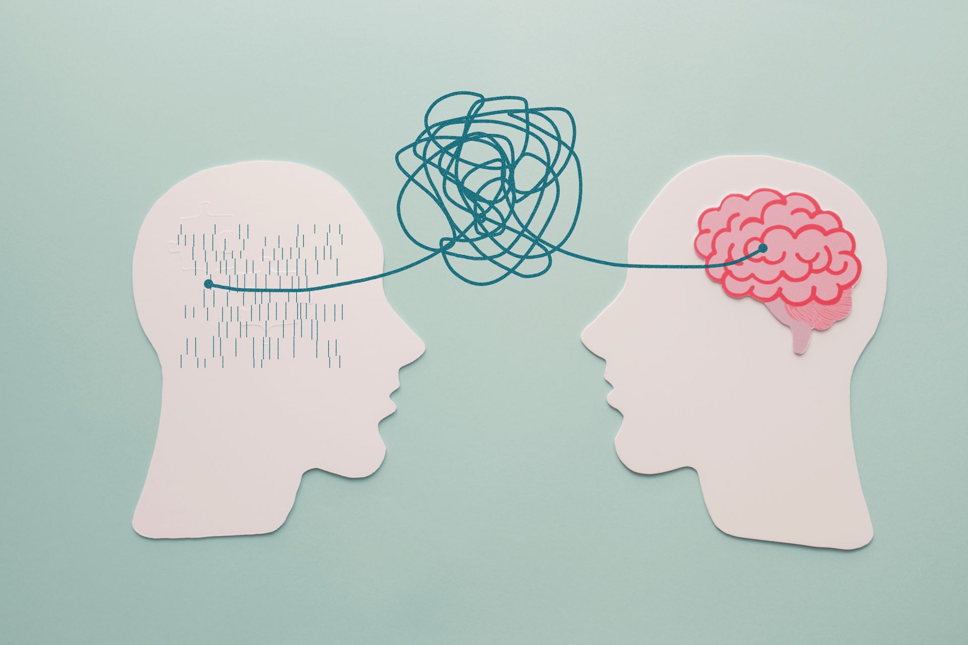 Deux têtes découpées en papier avec une ficelle emmêlée entre elles, une tête a un graphique de cerveau, l'autre a des cheveux.