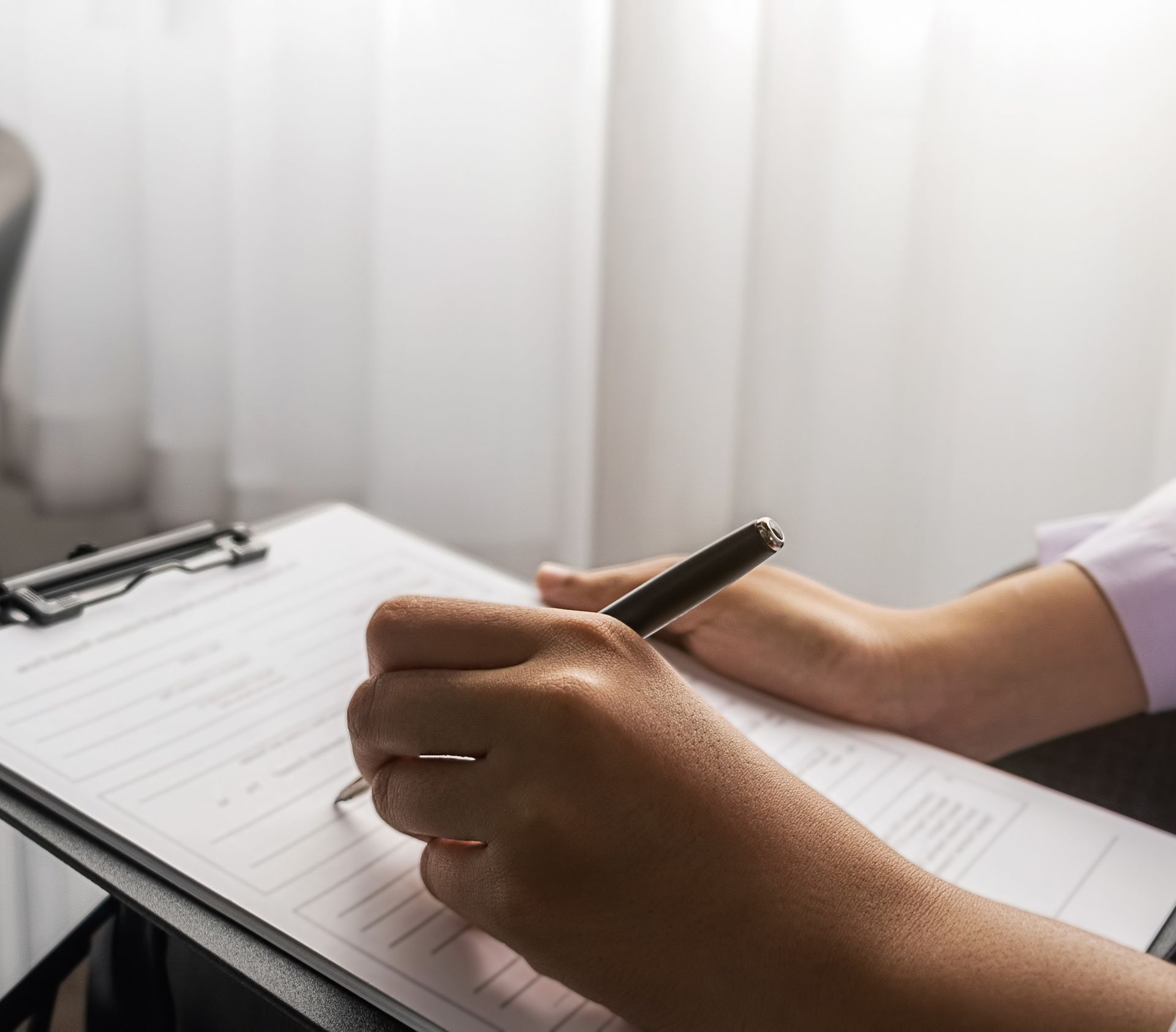 Personne écrivant sur un presse-papiers, assise près d'une fenêtre.