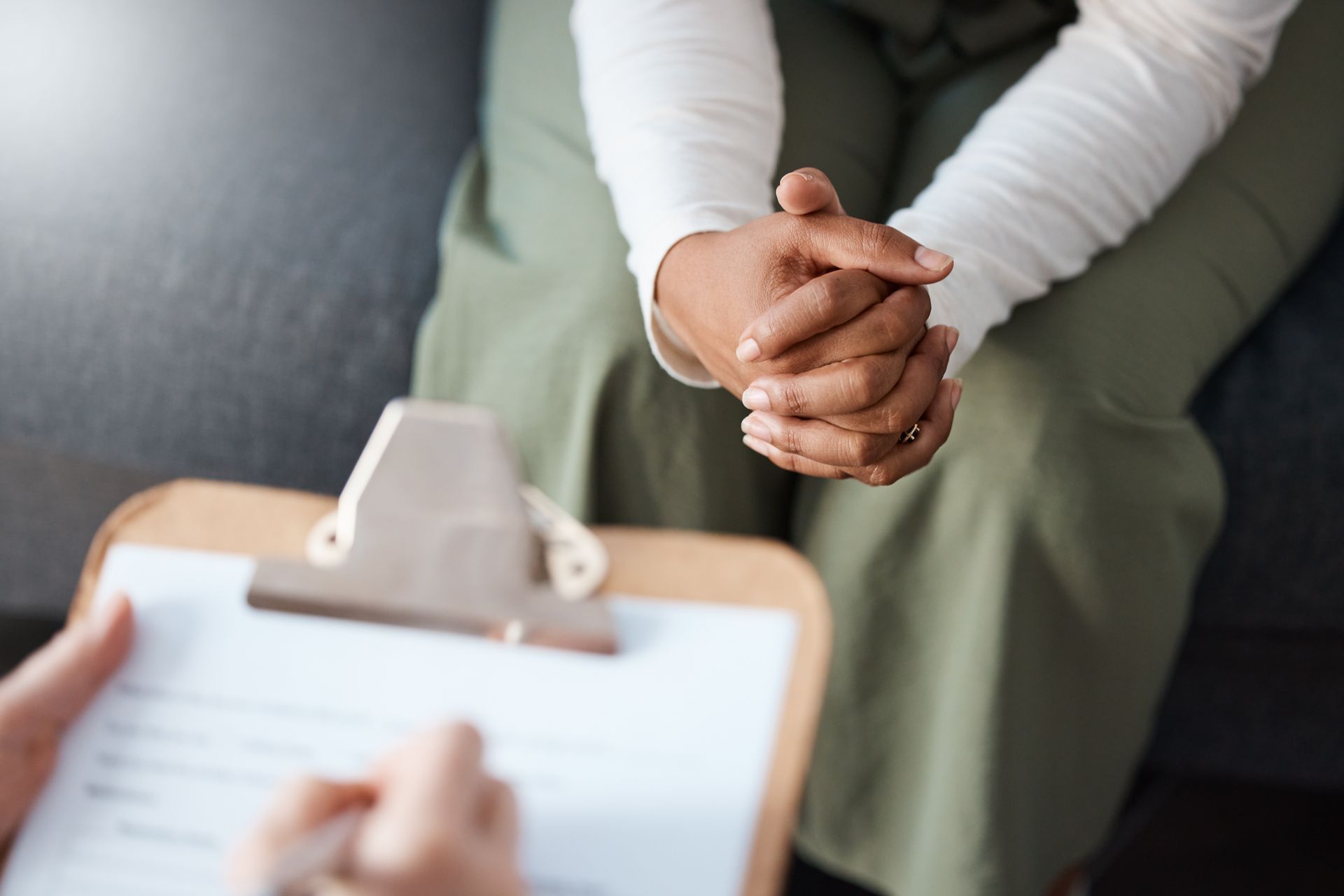 Personne assise, les mains jointes, face à quelqu'un qui prend des notes sur un presse-papiers.