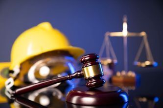 Mazo de juez frente a un casco amarillo y una balanza, símbolos de la ley y la seguridad en la construcción.