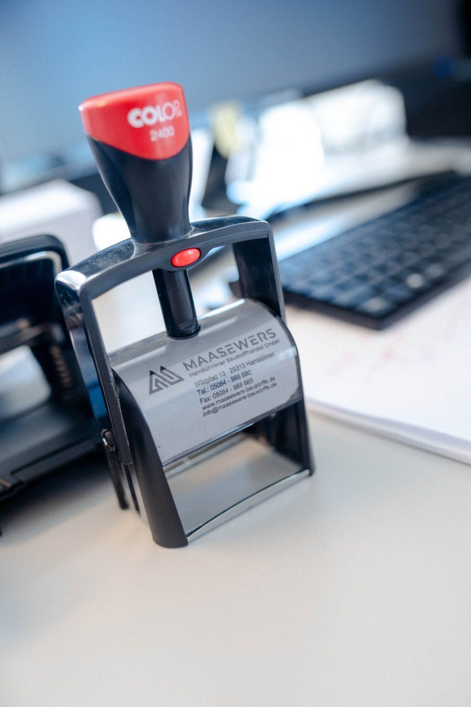Schwarze Jacke mit „MAASEWERS“-Logo über einem Stuhl in einem hellen Büroumfeld.