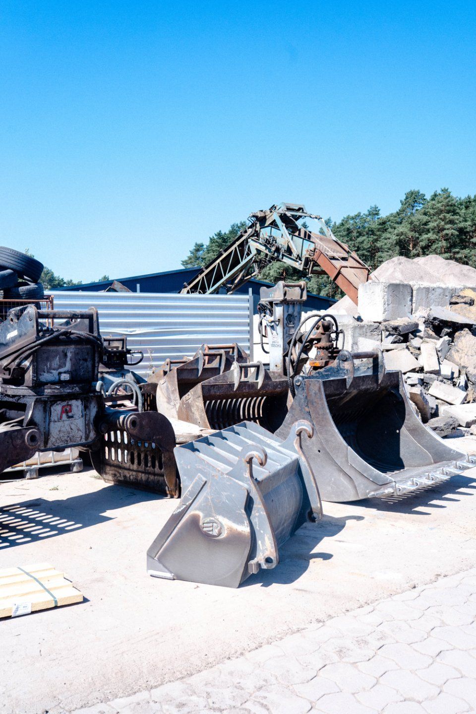 Kies- und Steinhaufen auf einem Baustoffhof, im Hintergrund ein Gebäude und Bäume.