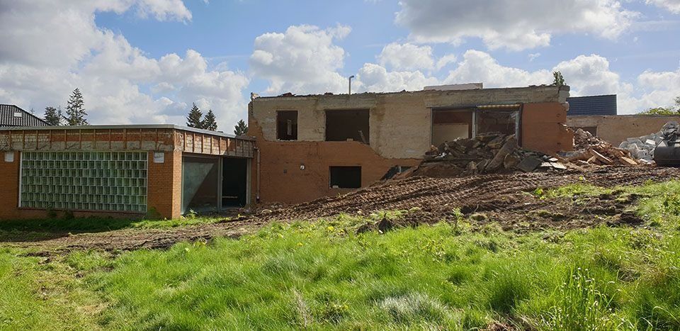 Ein Gebäude wird abgerissen, auf dem Boden liegen Trümmer und im Vordergrund grünes Gras.