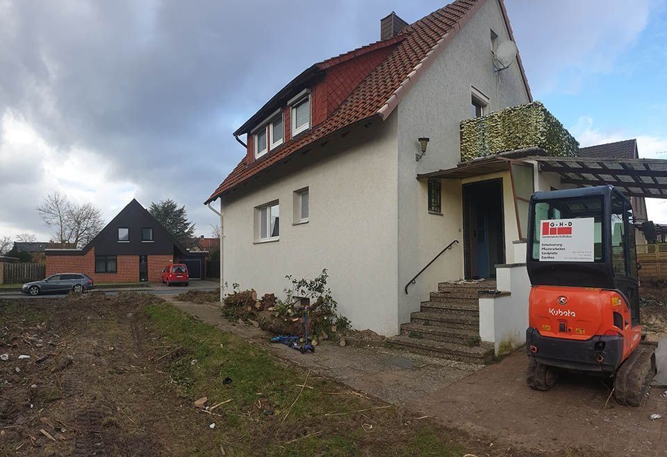 Haus wird renoviert, im Vordergrund Baumaschinen, bewölkter Himmel.