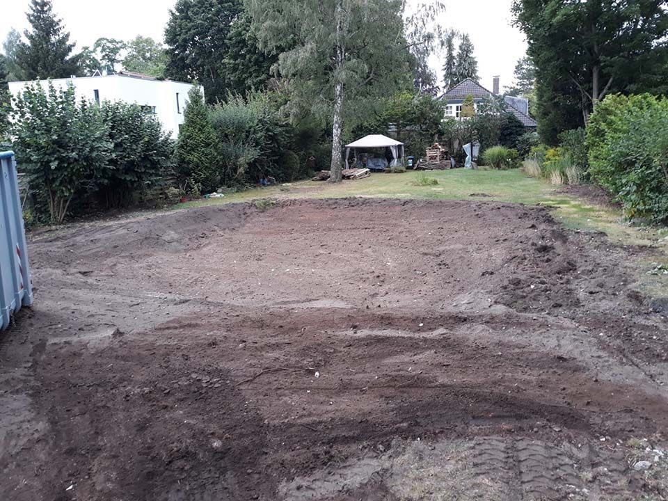 Geräumte Erde in einem Garten, bereit zum Bepflanzen. Häuser und Bäume im Hintergrund an einem bewölkten Tag.