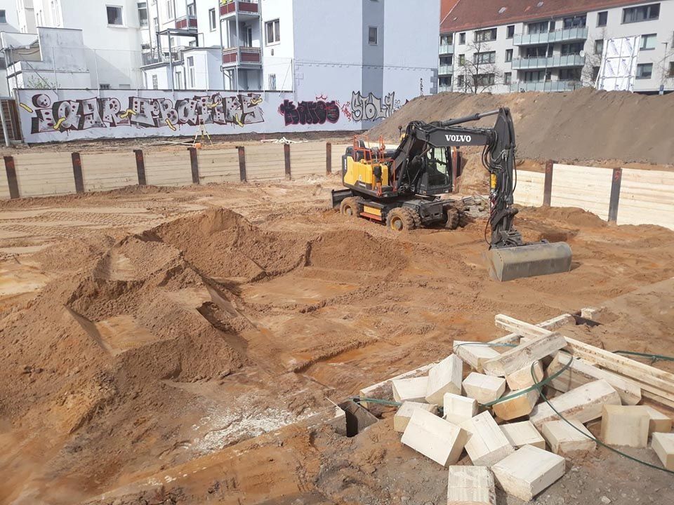 Bagger auf einer Baustelle, der Erde bewegt. Holzstützen und Steinhaufen.