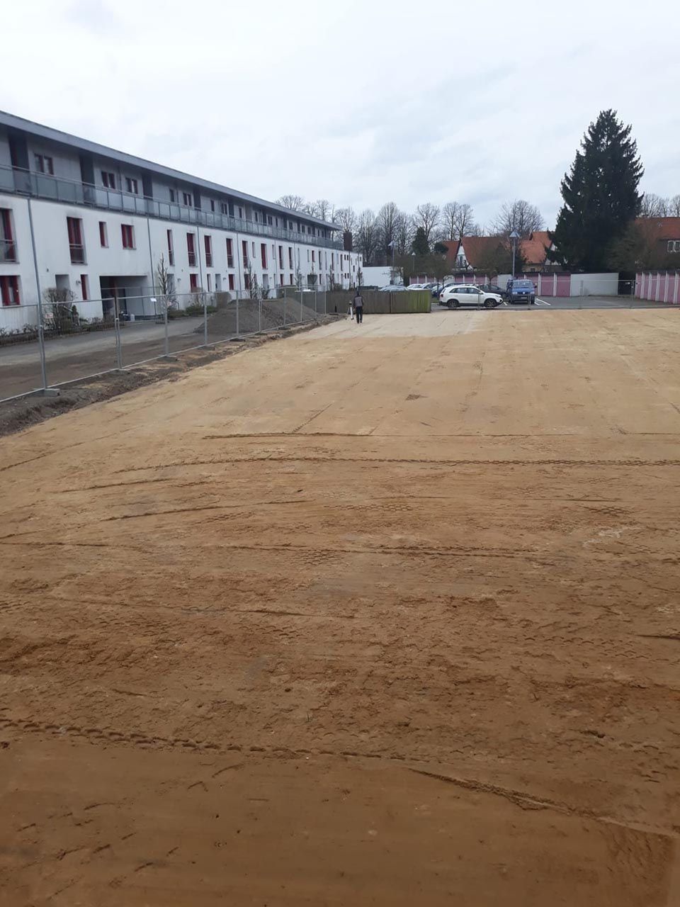 Ein leeres, braunes Feld vor einem langen, weißen Wohnhaus an einem bewölkten Tag.