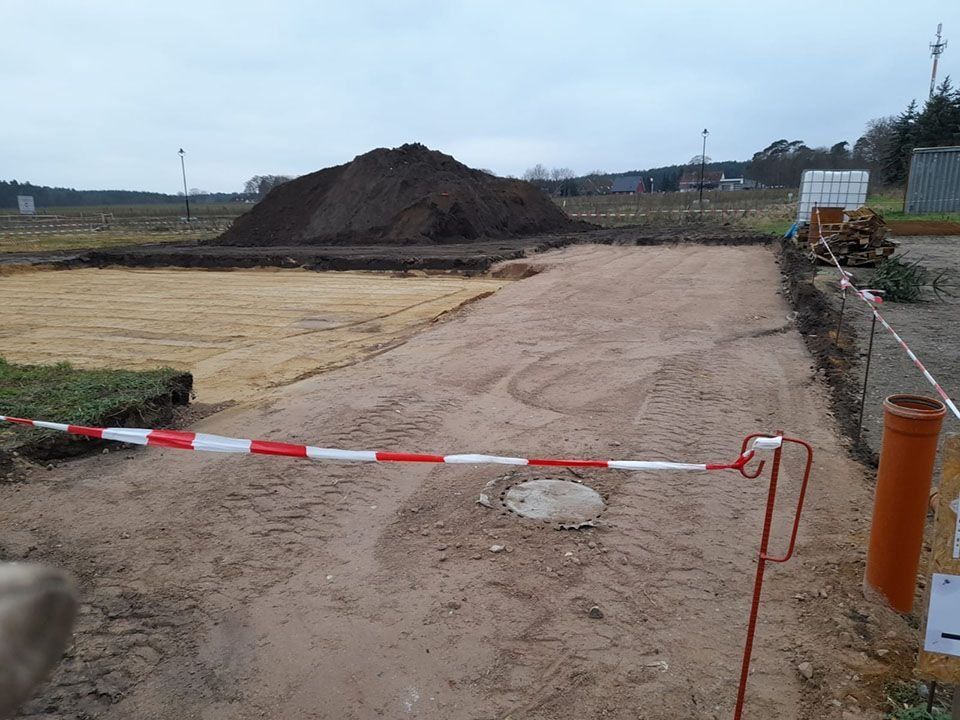 Baustelle mit Erdhaufen, Sand und einer rot/weißen Absperrung.