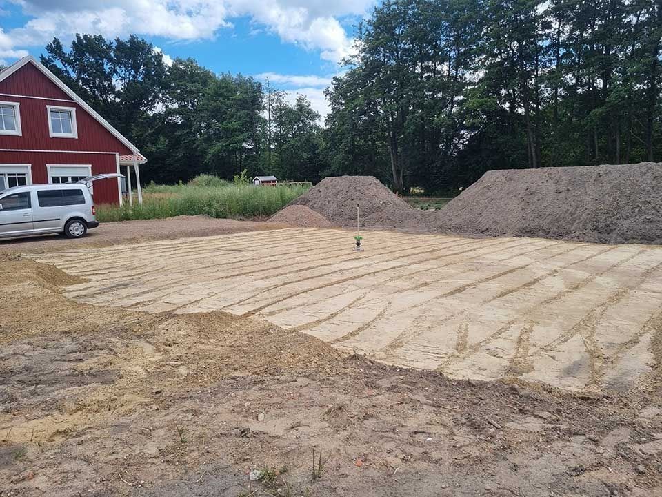 Baustelle mit ebenem Boden, Kieshaufen, einem roten Haus und einem weißen Lieferwagen.