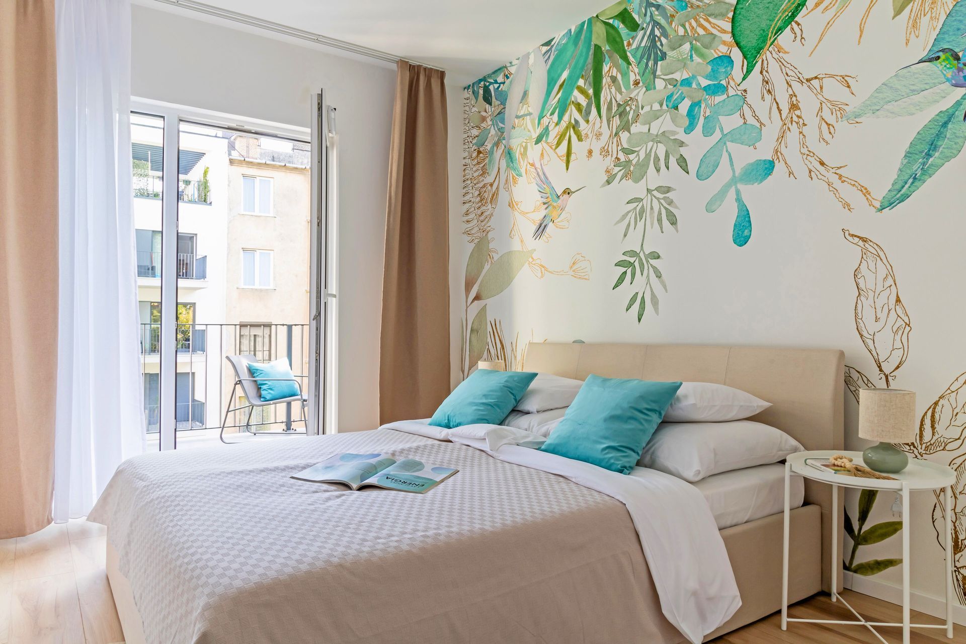 Bedroom with large bed, teal pillows, floral mural wall, balcony in Marone Colibri apartment in Budapest.