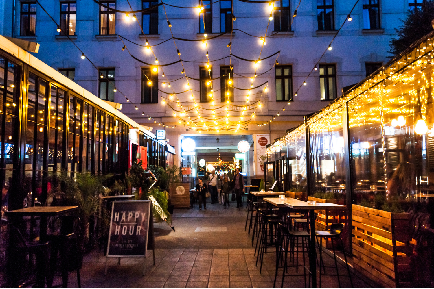 Outdoor evening scene of a courtyard with string lights and restaurants in Budapest Gozsdu Court. 