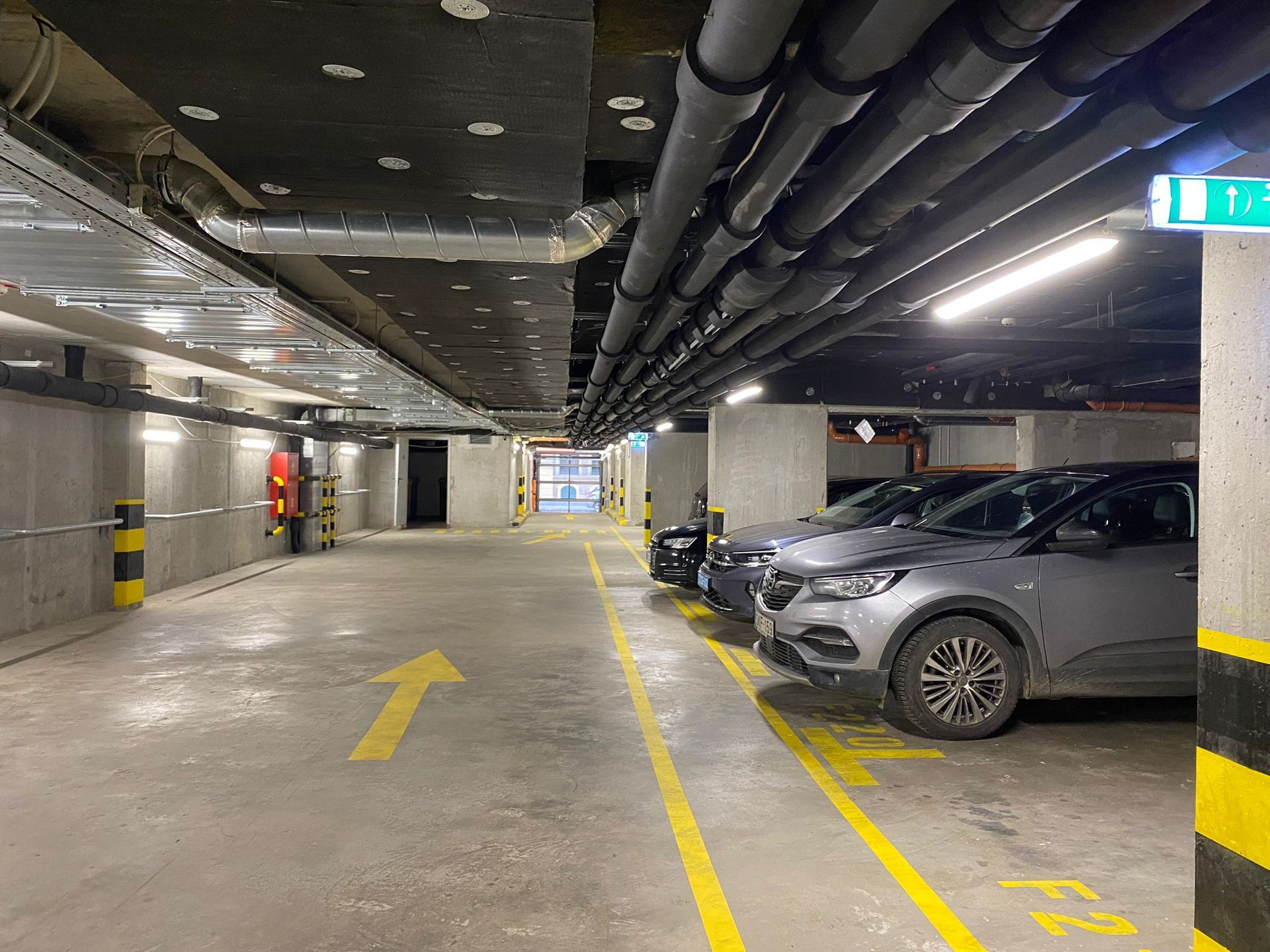 Indoor parking garage of Marone Parking with parked cars and yellow directional arrows.