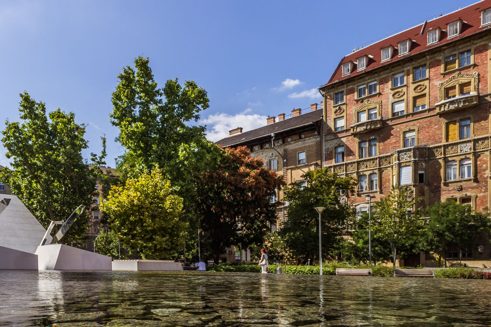 Rákóczi square, Budapest, Hungay, with reflecting pool, trees, and ornate building on a sunny day.