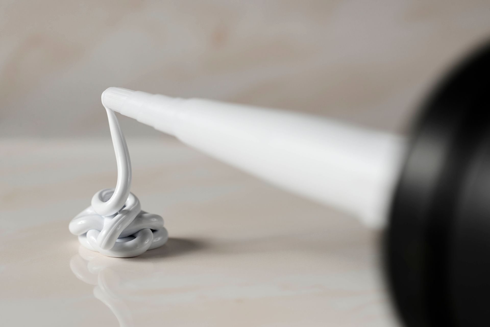 Weiße Dichtungsmasse oder Silikon wird aus der Düse eines schwarzen Applikatorrohrs auf eine helle Oberfläche aufgetragen.