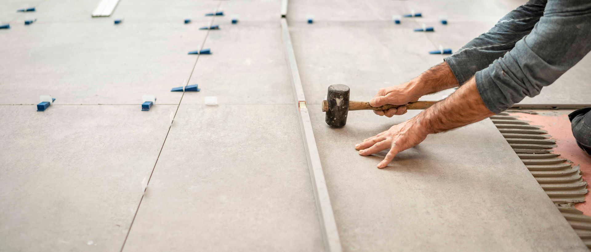 Eine Person klopft mit einem Gummihammer vorsichtig eine große Bodenfliese auf frischen Mörtel