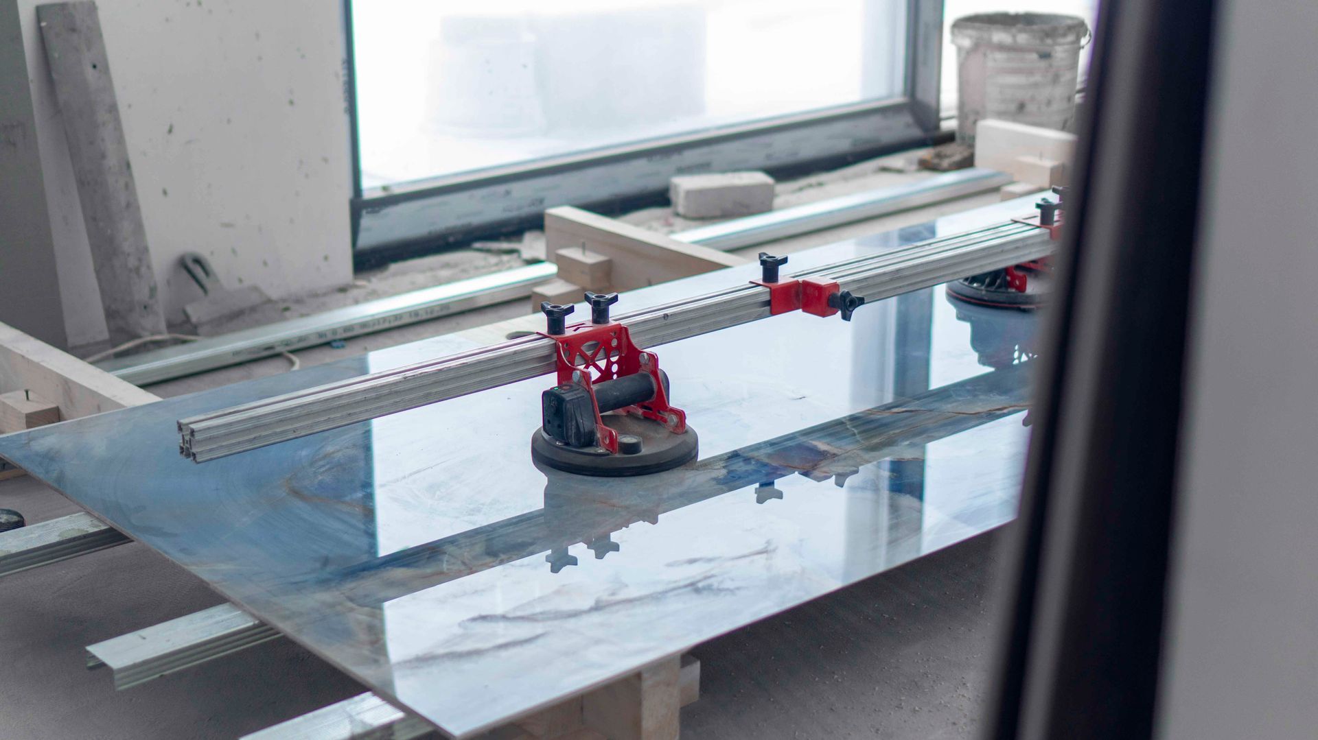 Eine Fliese wird auf einem Arbeitstisch mit speziellen roten Saugnapf-Hebevorrichtungen und Führungsschienen