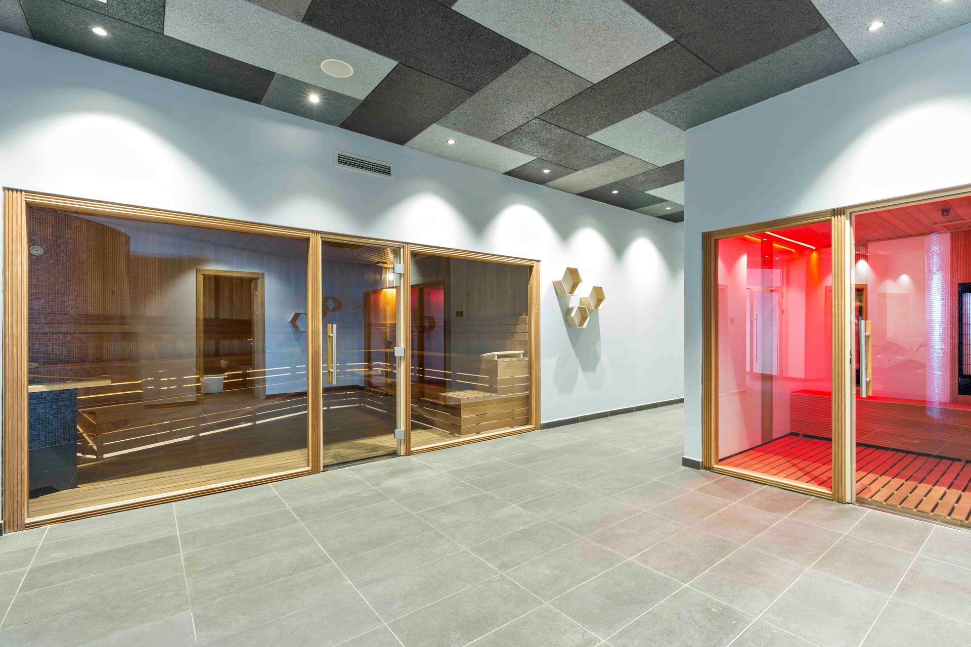 Ein moderner Spa-Bereich mit einer verglasten Sauna und einer Infrarotkabine, die in rotes Licht getaucht ist.