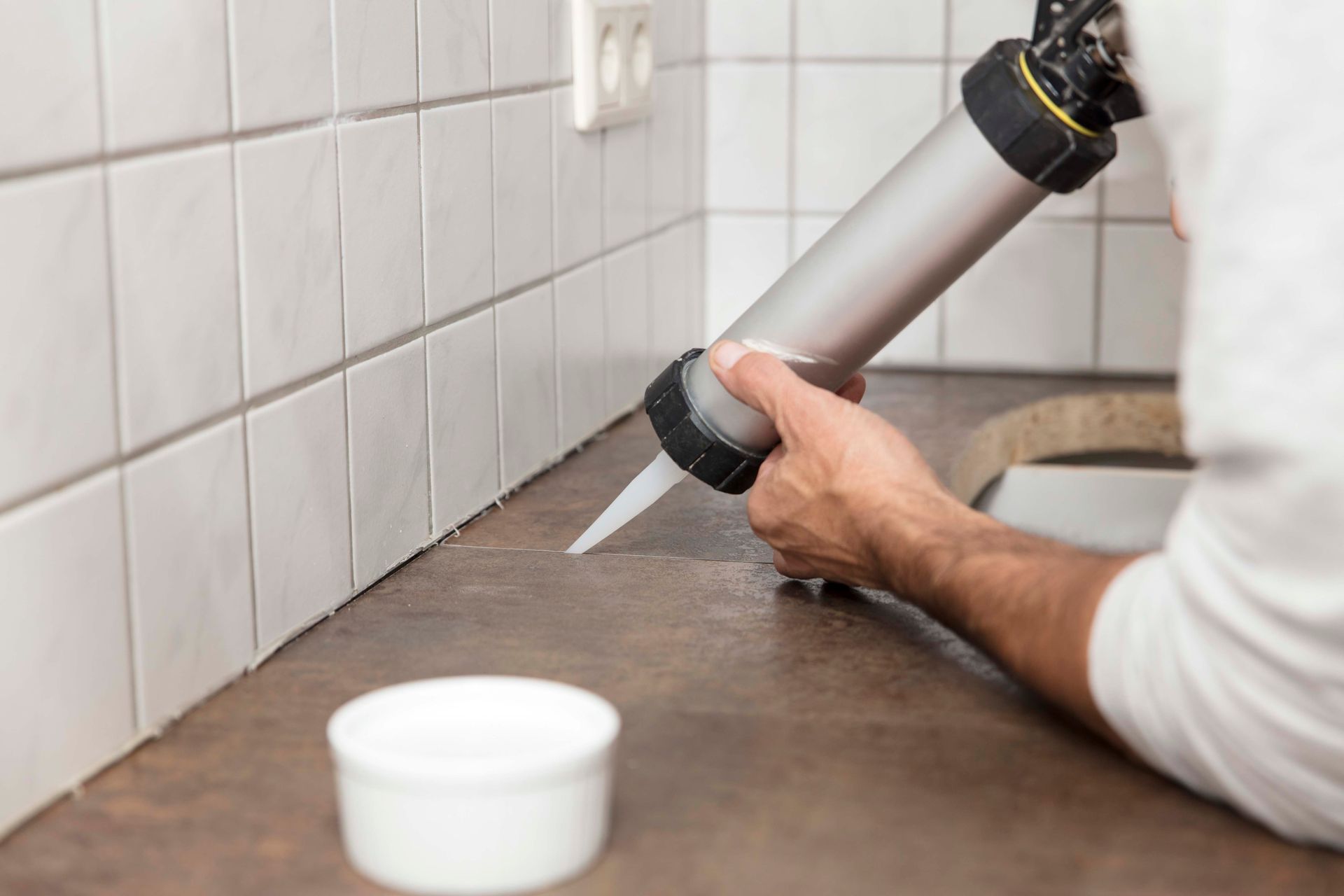 Eine Person trägt Silikondichtstoff mit einer Kartuschenpistole entlang der Fuge zwischen einer gefliesten Wand