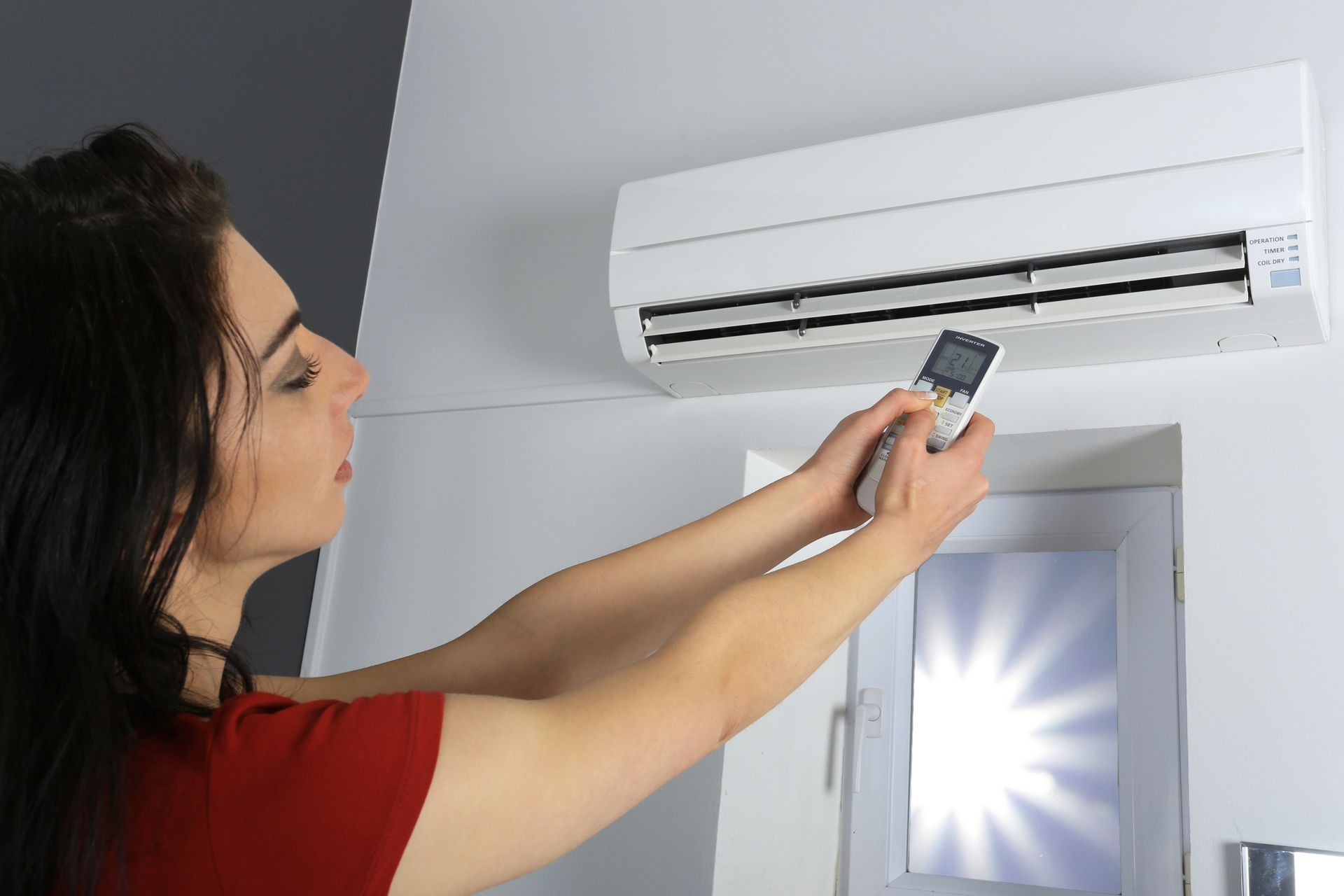 Femme utilisant la télécommande pour régler un climatiseur.